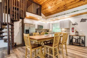 Eine moderne Küche mit weißen Schränken, einem Holzesstisch und einer Treppe mit Holzwandung.