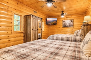 Une chambre de type cabane avec deux lits, un ventilateur de plafond, un téléviseur fixé au mur et une image d’ours accrochée au mur.