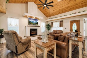 A living room with a fireplace, leather furniture, and a ceiling fan. - 5 King Bedroom Mtn Lodge Hot Tub, Yard, & Games (Sevierville)