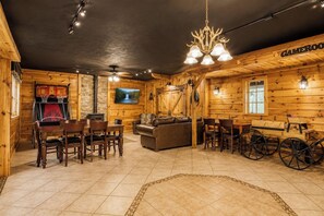 A cozy log cabin interior with a dining area, a leather couch, and a television mounted on the wall. - 5 King Bedroom Mtn Lodge Hot Tub, Yard, & Games (Sevierville)