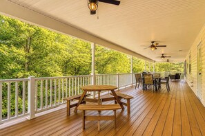 Eine überdachte Holzterrasse mit Picknicktisch und Stühlen, umgeben von weißen Geländern, mit Blick auf ein bewaldetes Gebiet.