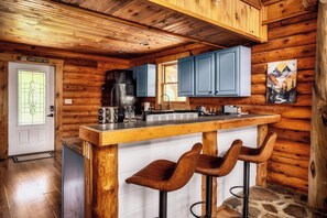A wooden cabin interior with a kitchen area, bar stools, and a door labeled 'Home Sweet Home.' - Family Retreat! Private Pool, Hot Tub, Game Room! (Sevierville)