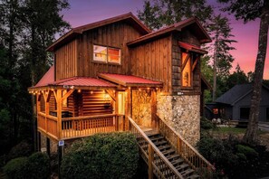 A wooden cabin with a porch, stone foundation, and a staircase leading to the entrance. - Family Retreat! Private Pool, Hot Tub, Game Room! (Sevierville)