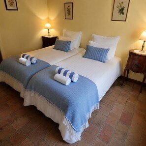 Ein Doppelbett mit einer blau-weiß gestreiften Decke und zwei aufgerollten Handtüchern. Zwei Nachttische mit Lampen stehen bereit, und der Raum verfügt über einen Fliesenboden.