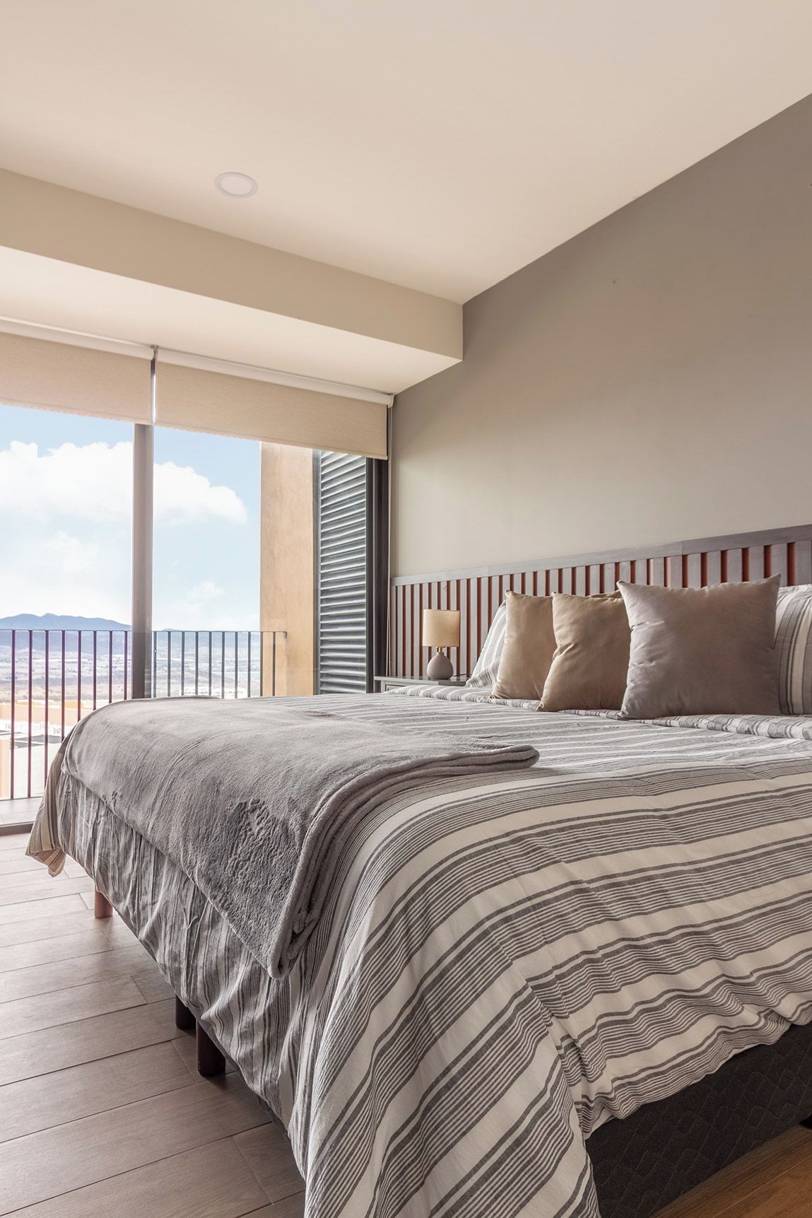A modern bedroom with a large bed, a nightstand, and a view of the outdoors.