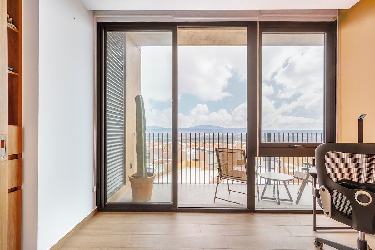 Een balkon met uitzicht op de lucht en een landschap in de verte, een stoel en een tafel.