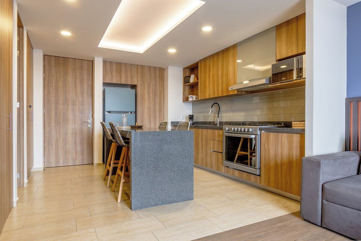 A modern kitchen with wooden cabinets, a central island, and a built-in oven.
