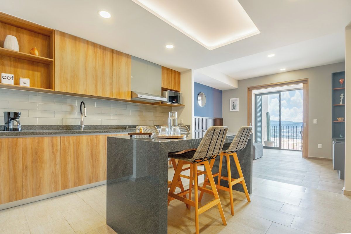 A modern kitchen with wooden cabinets, a granite countertop, and a bar area with two bar stools.