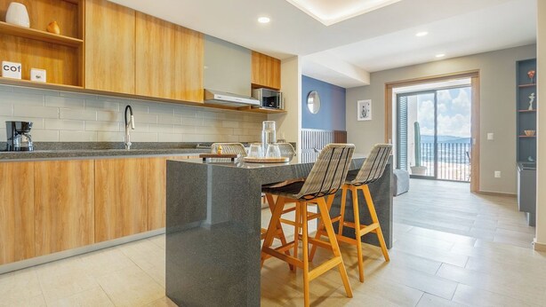 Eine moderne Küche mit Holzschränken, einer Granit Arbeitsplatte und einer Bar mit zwei Barhocker.