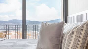 Un lit avec une literie à rayures et une vue sur un paysage montagneux, visible à travers de grandes fenêtres.