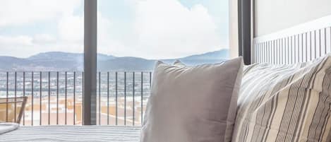 A bed with striped bedding and a view of a mountainous landscape through large windows.