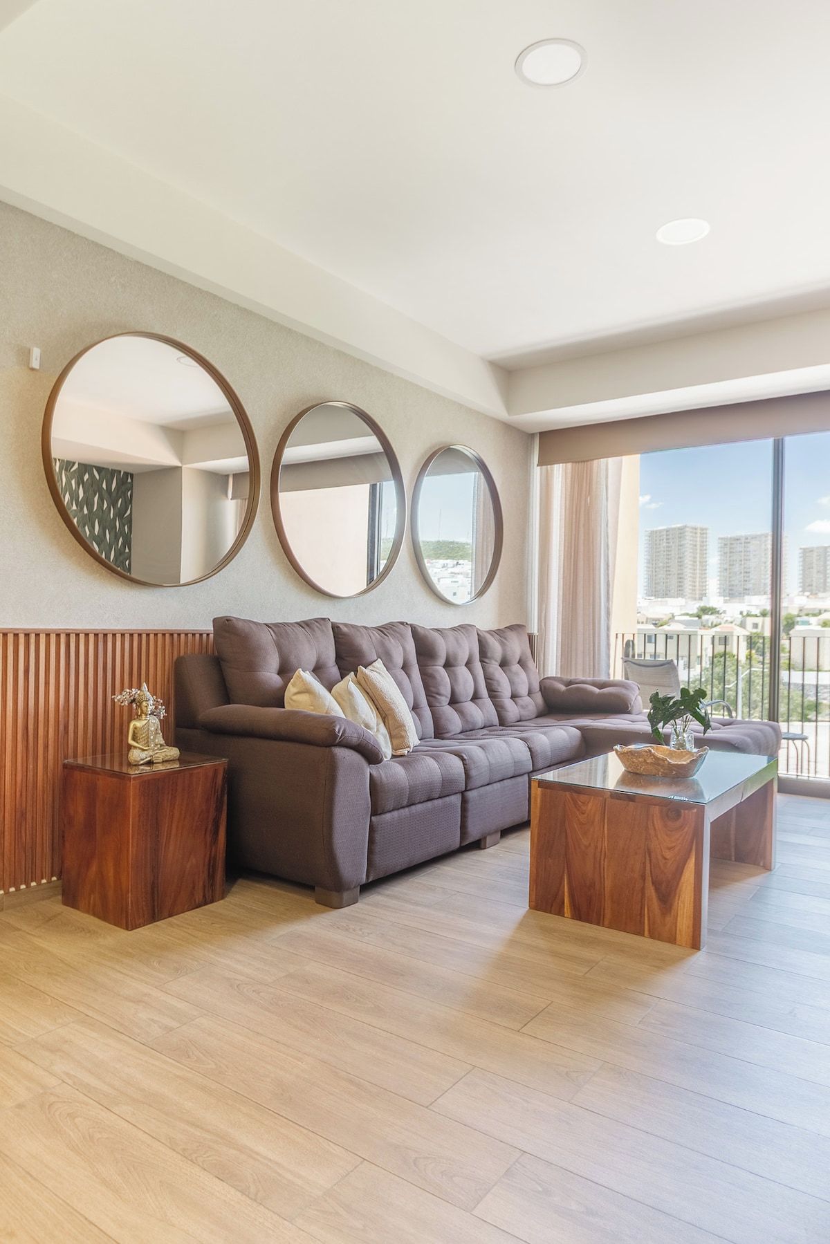 A modern living room with a large sofa, two side tables, and three wall-mounted mirrors.
