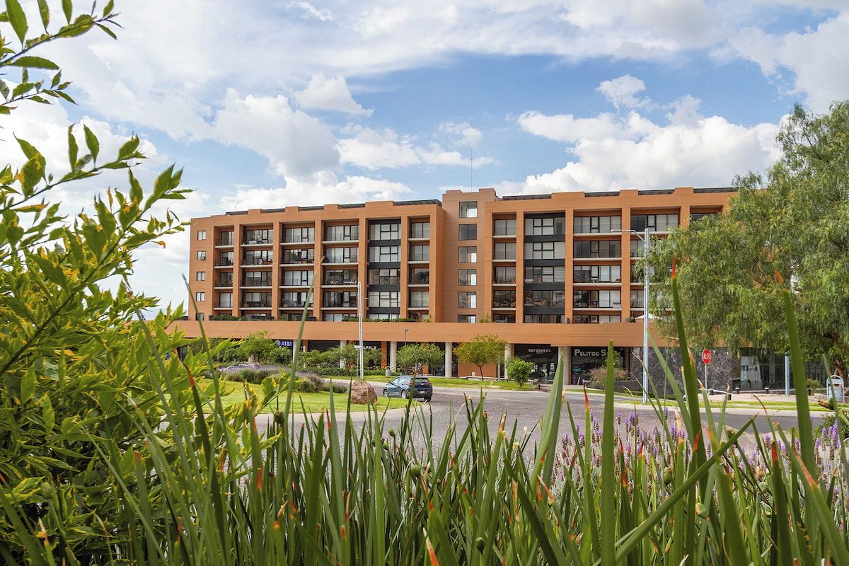 A multi-story building with a flat roof, large windows, and a parking area in front.