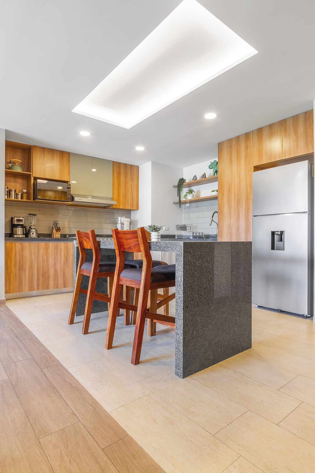 A modern kitchen with wooden cabinetry, a granite countertop island, and a stainless steel refrigerator.