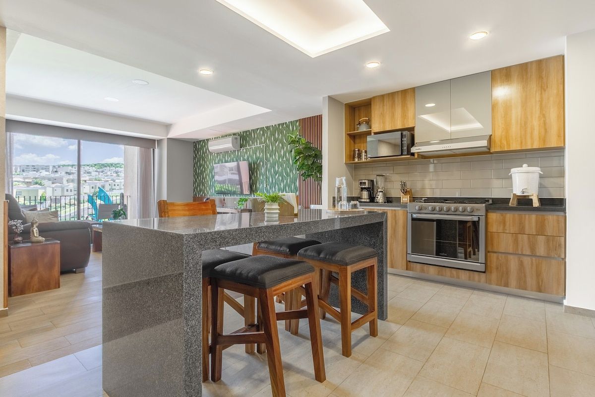 A modern kitchen with a central island, bar stools, and a view of the city.