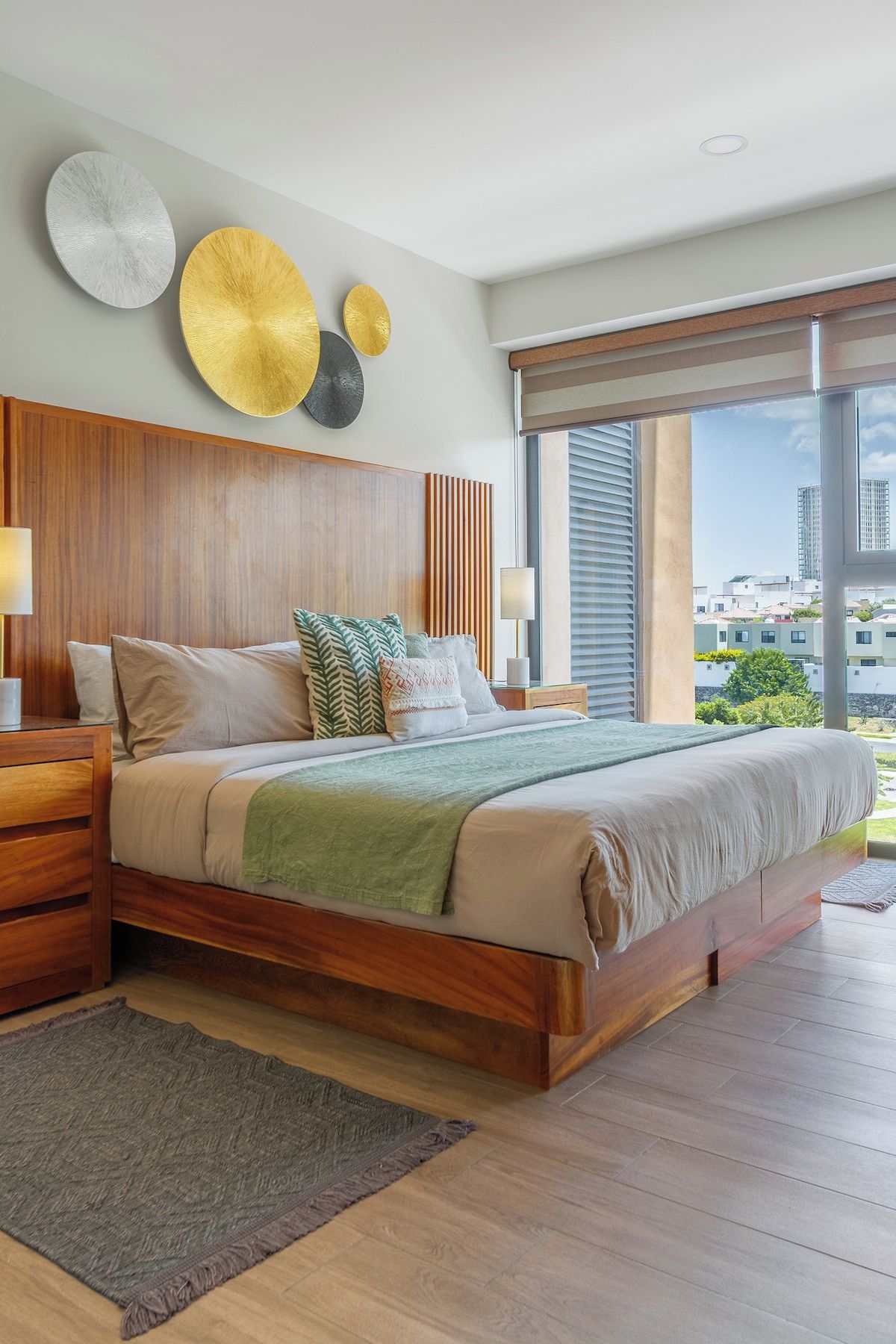 Quarto moderno com cama grande, cabeceira de madeira e vista para a cidade.