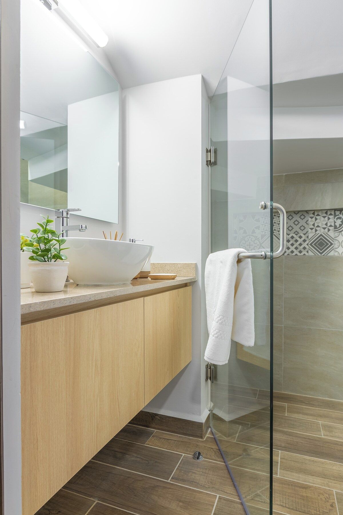 A modern bathroom with a glass shower enclosure, a white sink, and a wooden vanity.