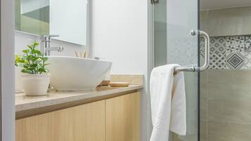 A modern bathroom with a glass shower enclosure, a white sink, and a wooden vanity.