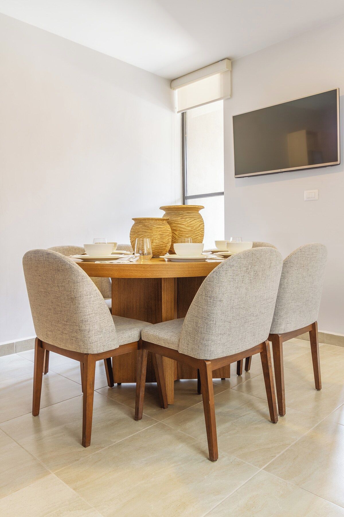Een eetgedeelte met een ronde tafel, vier stoelen en een aan de muur bevestigde televisie.