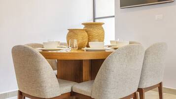 Een eetgedeelte met een ronde tafel, vier stoelen en een aan de muur bevestigde televisie.