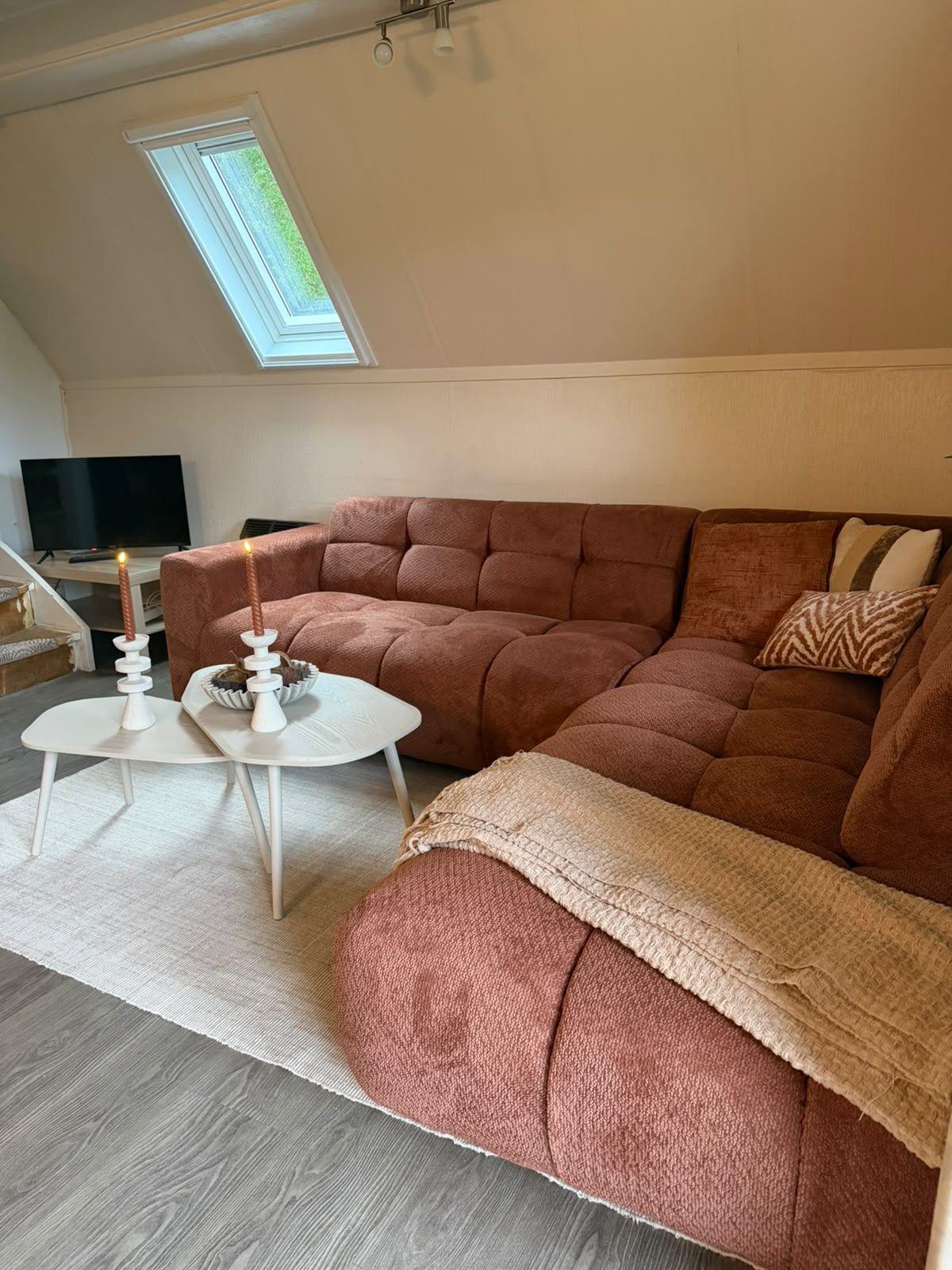 A cozy living room with a sectional sofa, a small white table, and a television.