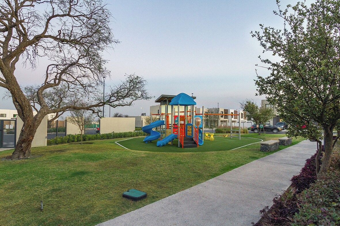 A playground with slides and climbing structures, surrounded by a grassy area and a paved path.