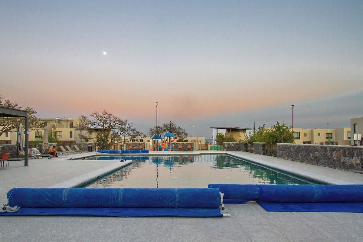 A swimming pool area with lounge chairs and umbrellas, surrounded by buildings.