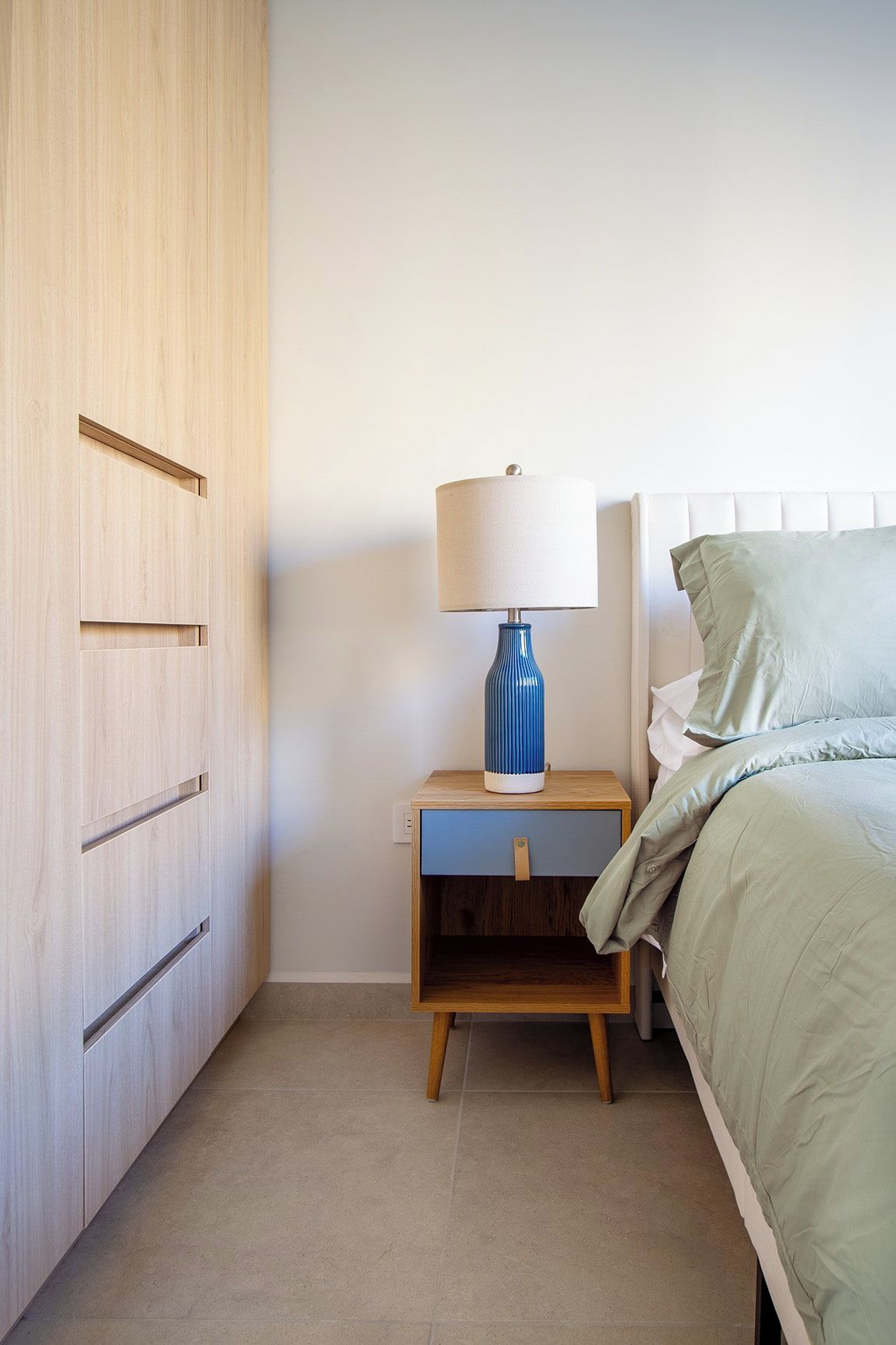 A bedroom with a bed, a nightstand with a lamp, and a wooden wardrobe.