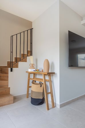 Ein modernes Interieur mit einer Treppe, einem Holztisch mit Dekoration, einem gewebten Korb und einem wandmontierten Flachbildfernseher.