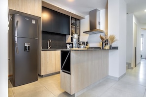 Une cuisine moderne dotée d’un réfrigérateur encastré, de meubles de rangement aux couleurs sombres et d’un îlot central avec un évier.
