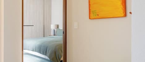 Un couloir menant à une chambre à coucher, où se trouvent un lit, un tableau accroché au mur et une plante en pot.
