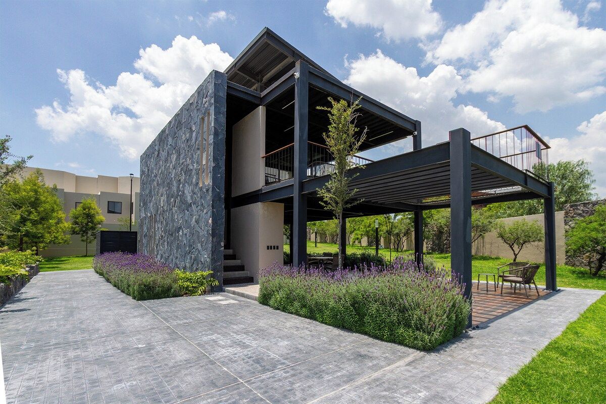 A modern building with a stone facade, a covered outdoor seating area, and a clear sky.