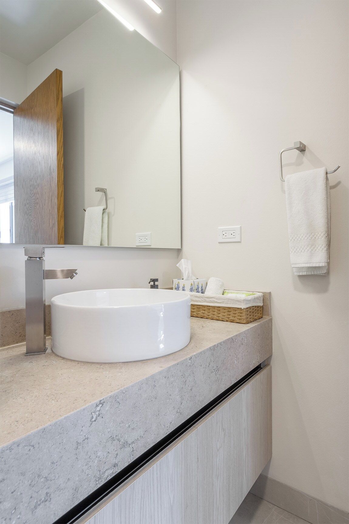 Un baño con un lavabo blanco redondo, un espejo, un perchero y una cesta con artículos de aseo.