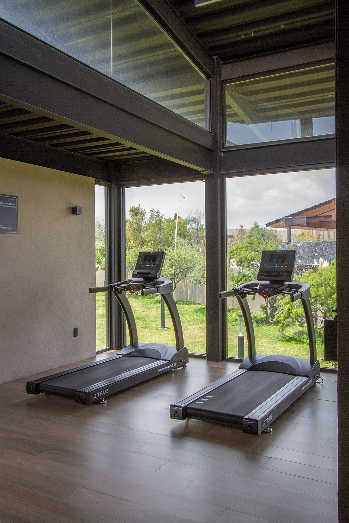 Ein Fitnessraum mit zwei Laufbändern, einer Steuerung und Blick auf Grünfläche.