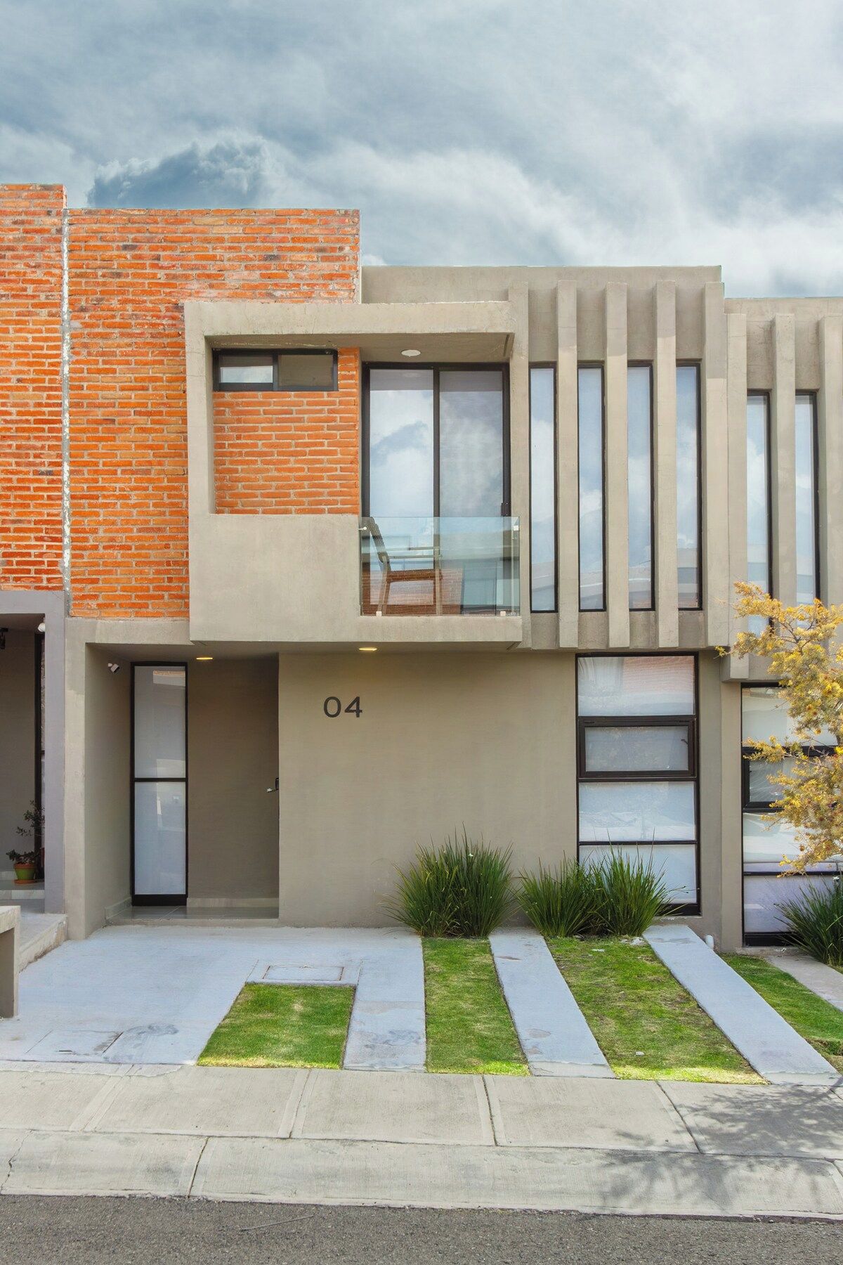 A modern two-story residential building with a brick facade, large windows, and a flat roof.