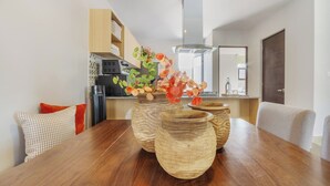 Ein Essbereich mit einem Holztisch, drei Keramikvasen mit Blumen und einer Küche im Hintergrund.
