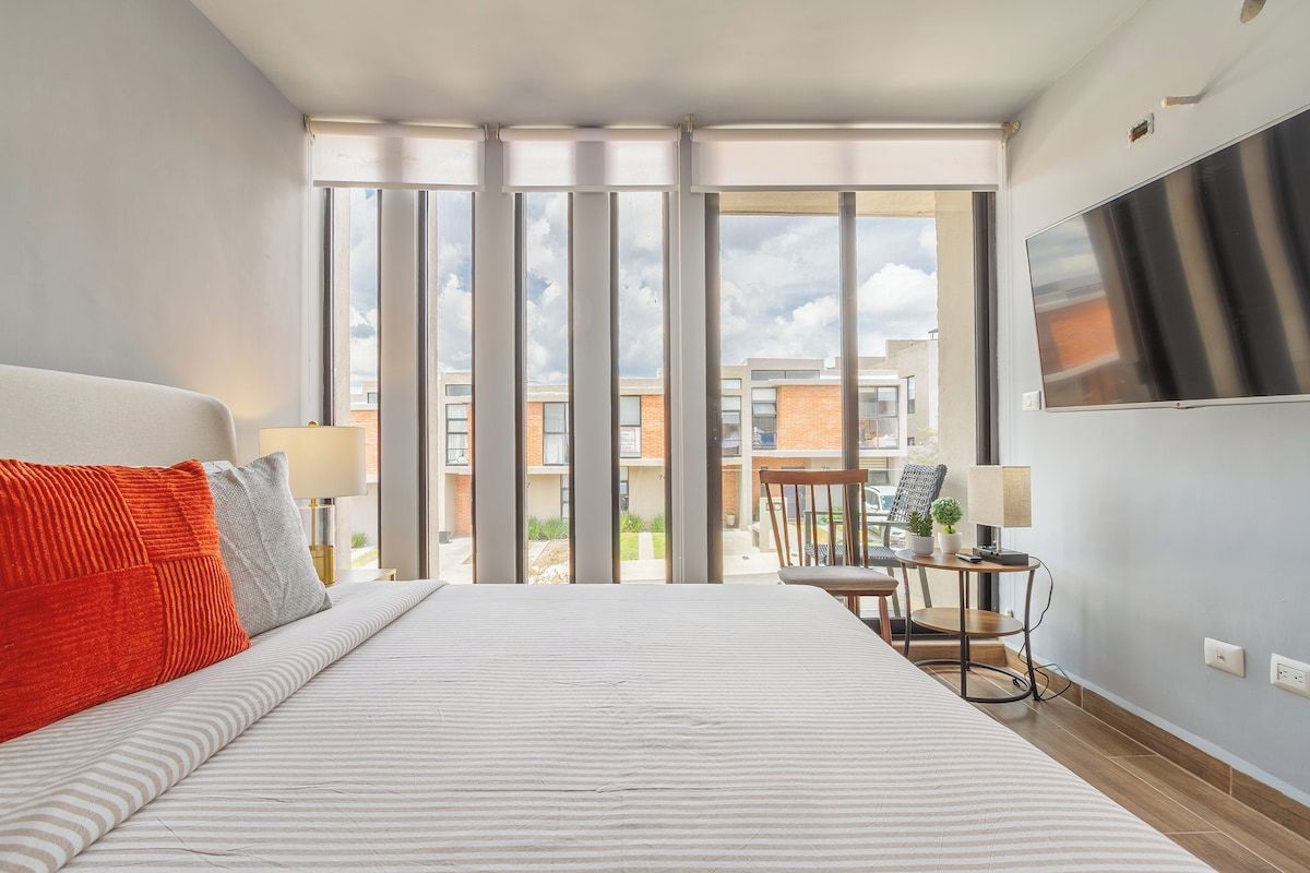 Une chambre d’hôtel avec un grand lit, un téléviseur fixé au mur et un balcon offrant une vue sur les immeubles.