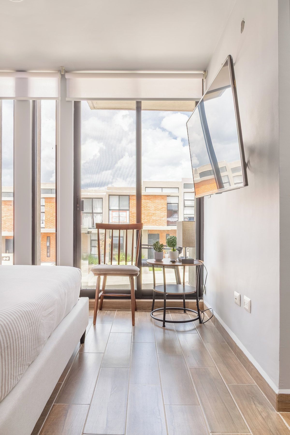 A modern bedroom with a large bed, a chair, a small table, and a TV mounted on the wall.
