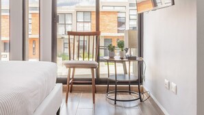 Ein modernes Schlafzimmer mit einem großen Bett, einem Sessel, einem kleinen Tisch und einem an der Wand befestigten Fernseher.