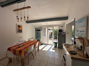 A dining area with a table and chairs, a kitchen with appliances, and a door leading to an outdoor space. - Villa for 4–5 people on the Valcros hillside, with a magnificent view and a private pool (La Londe-les-Maures)