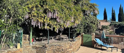A pool area with stone walls, a lounge chair, and a pergola with hanging plants.
