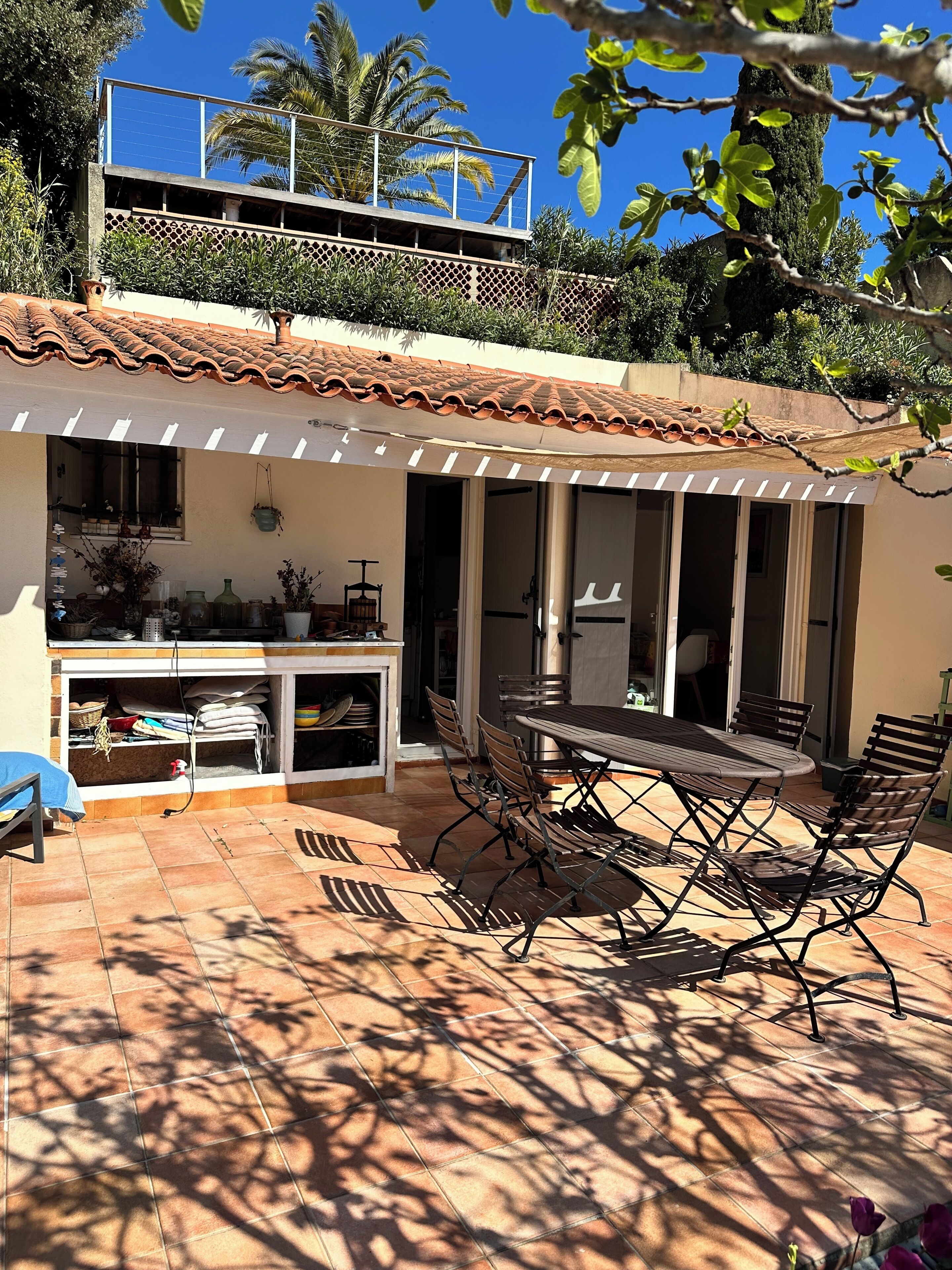 A patio with a table and chairs, a covered area with a railing, and a view of a building with a tiled roof.