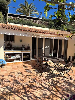 A patio with a table and chairs, a covered area with a railing, and a view of a building with a tiled roof. - Villa for 4–5 people on the Valcros hillside, with a magnificent view and a private pool (La Londe-les-Maures)