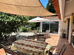 Eine Terrassengruppe im Freien mit Tisch, Stühlen und einem großen Sonnenschirm, mit Blick auf den Garten.