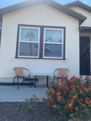 A building with two windows, a door, and a small outdoor seating area with chairs and a table. - Alabama Abode - Newly Remodeled (San Diego)
