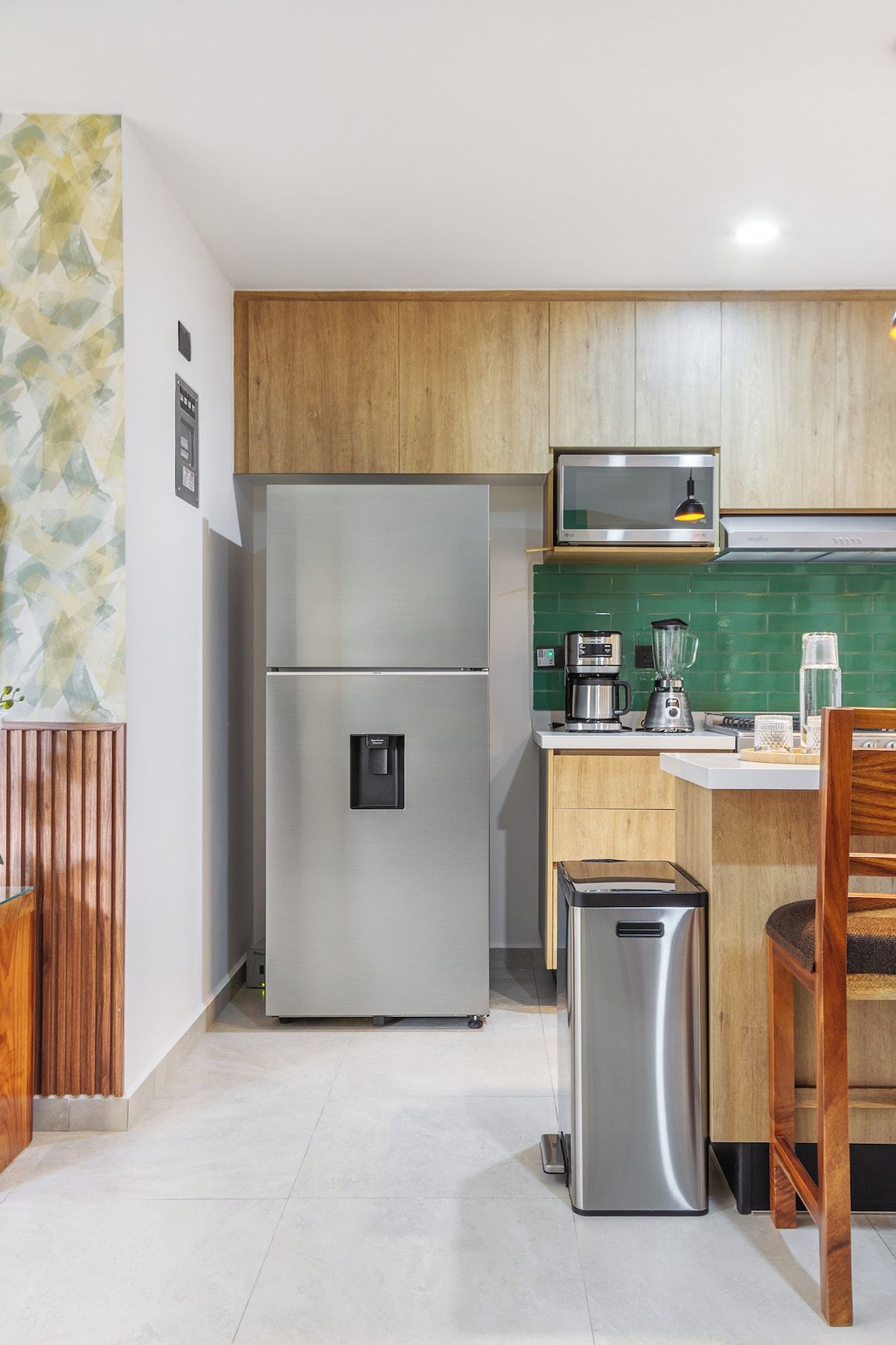 Cozinha compacta com geladeira de aço inoxidável, micro-ondas e cafeteira na bancada.