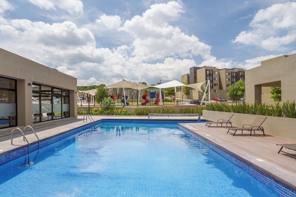 A swimming pool with a tiled deck, lounge chairs, and a playground in the background.