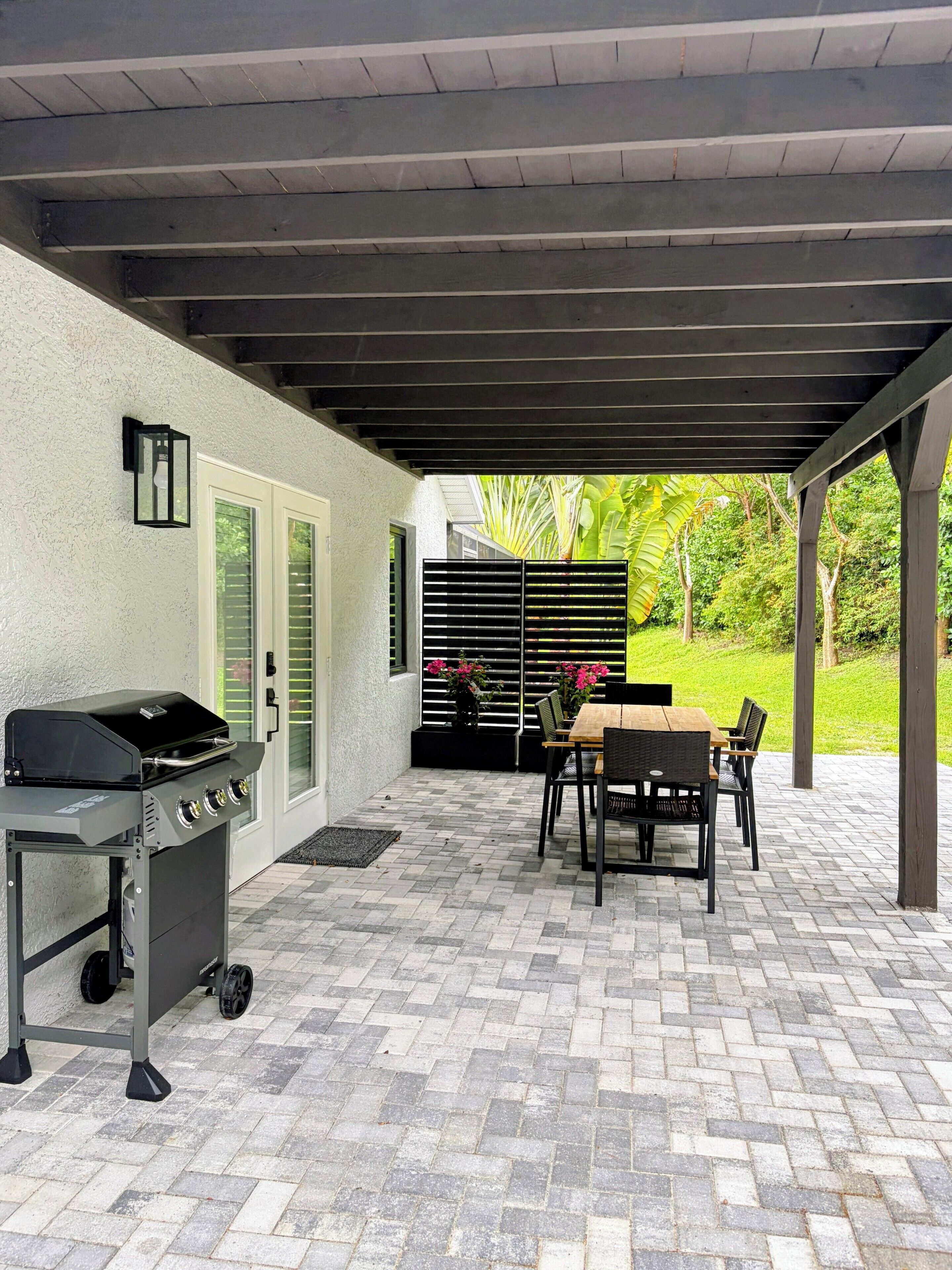 Un patio exterior con una parrilla, una mesa con sillas y una zona cubierta con vistas a la vegetación.