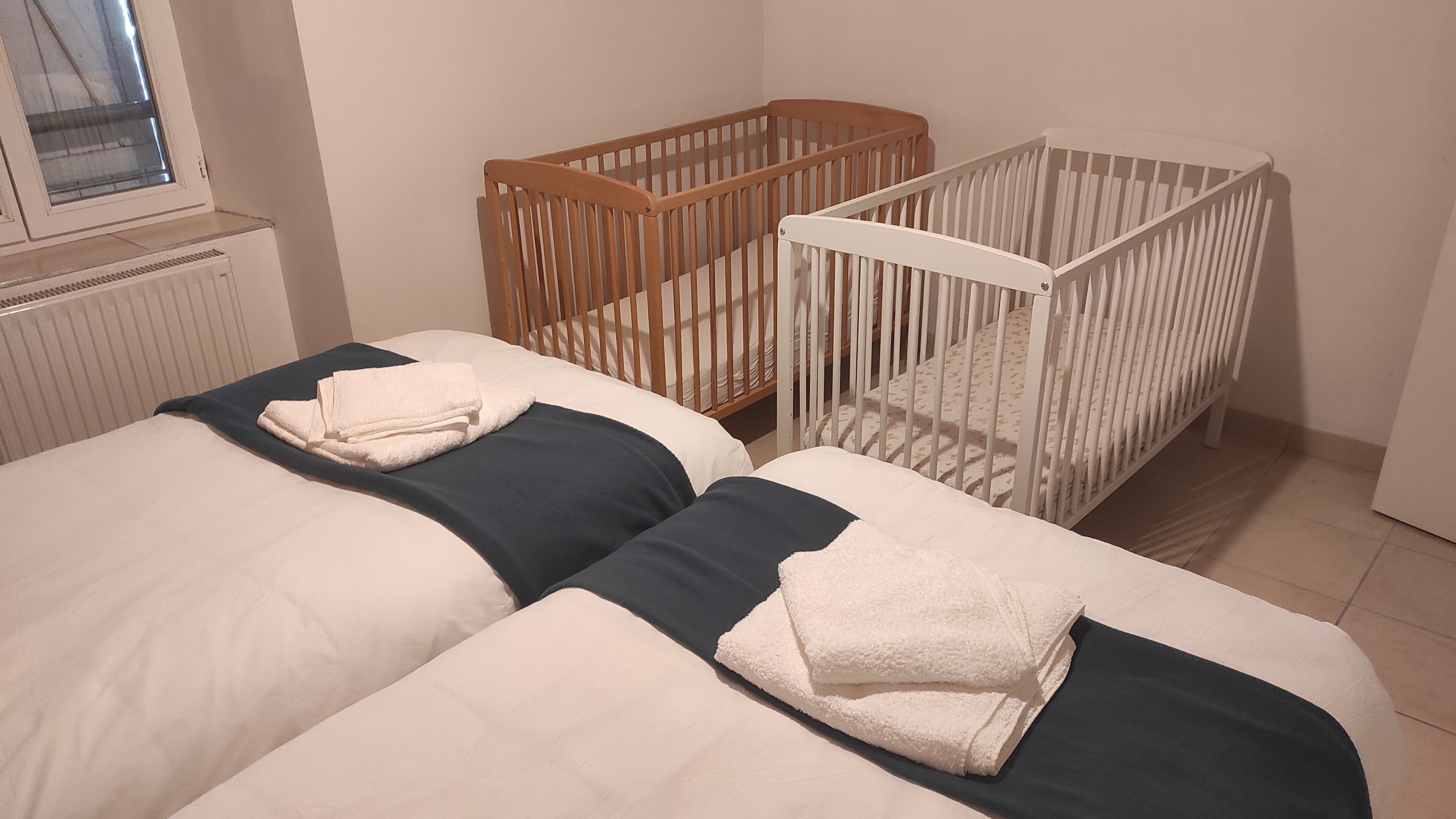 Une chambre avec deux lits, un berceau en bois et un berceau blanc.
