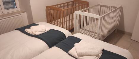 A bedroom with two beds, a wooden crib, and a white crib.
